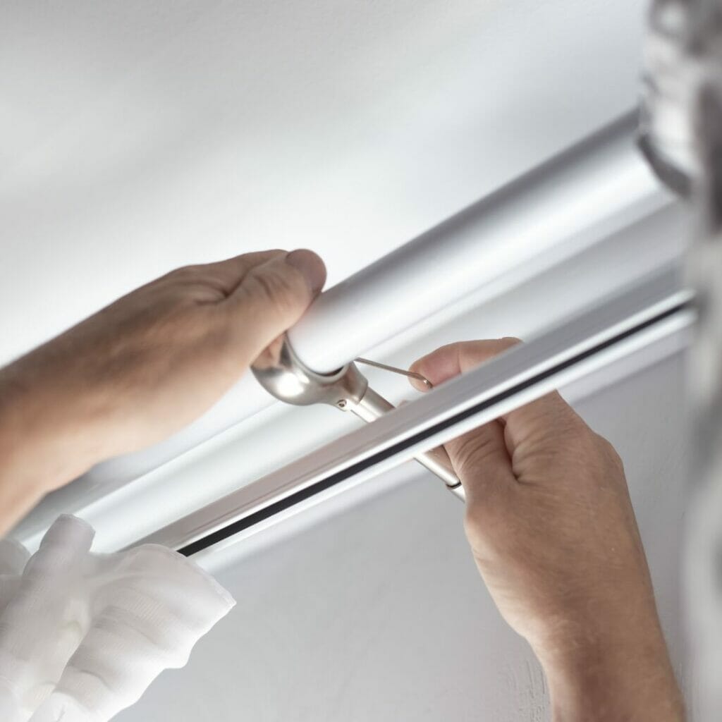 A man fixing a curtain rod in a bathroom.