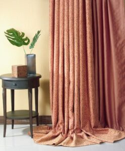 Beige Curtains Pool On The Floor Beside A Dark Wooden Round Table With A Glass Vase Holding Green Leaves.