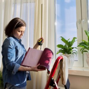 A Person Measuring A Window With A Tape While Holding Fabric Samples. A Ladder And Potted Plants Are Visible Nearby.